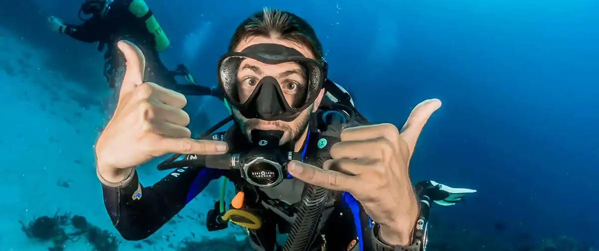 a male SCUBA diver close to the camera poses with hand signals